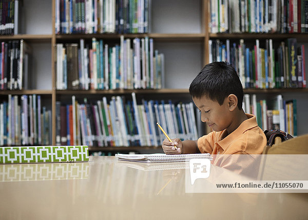 A boy sitting at table in a school library  using a pencil  studying.