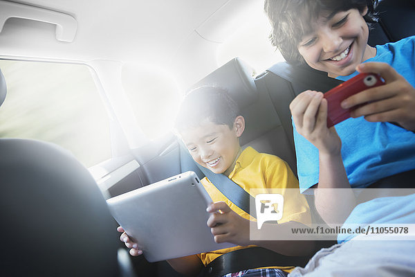 Two children travelling in the back seat of a car  one using a digital tablet and one a handheld game.