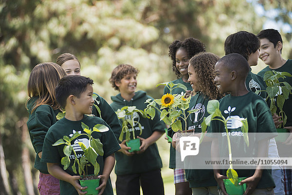 Kinder in einer Gruppe lernen etwas über Pflanzen und Blumen  tragen Pflanzen und Sonnenblumen.