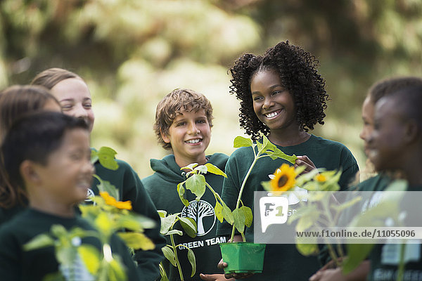 Kinder in einer Gruppe lernen etwas über Pflanzen und Blumen  tragen Pflanzen und Sonnenblumen.