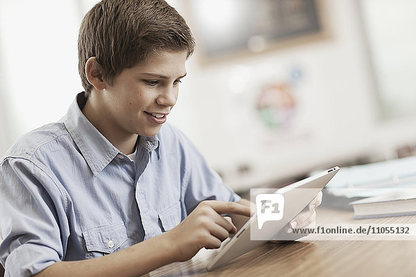 A boy sitting at a desk using a digital tablet.