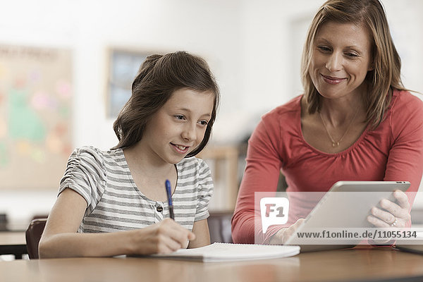 Eine erwachsene Lehrerin und ein Mädchen sehen sich ein digitales Tablet an.
