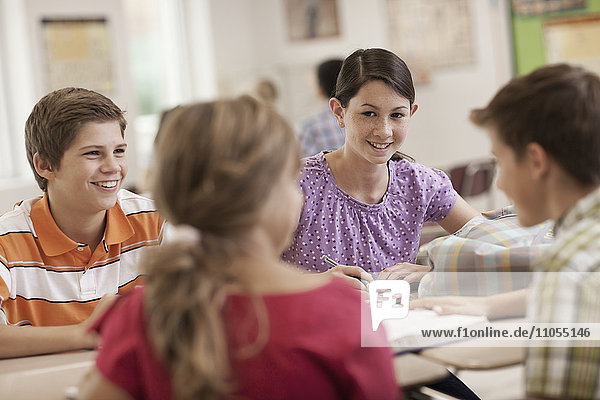 Eine Gruppe von Schülerinnen und Schülern  die in einer Unterrichtsstunde am Schreibtisch sitzen und miteinander reden.