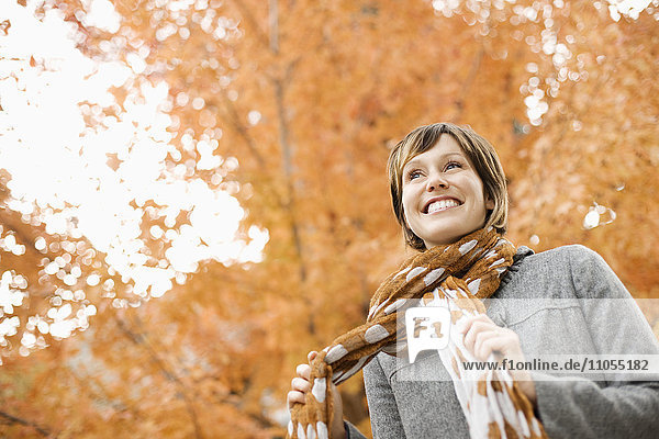 A woman in a jacket and neck scarf against a backdrop of autumn trees in vivid colour.