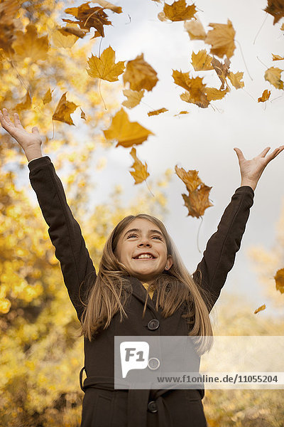 Ein Mädchen wirft gefallenes Herbstlaub in die Luft.