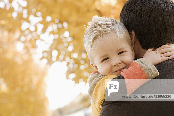 Ein erwachsener Elternteil und ein Kind  Vater und Sohn unter einem Baldachin aus orangefarbenem Herbstlaub.
