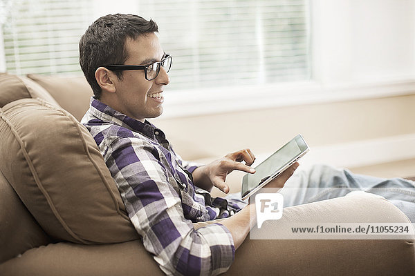 Ein Mann sitzt auf einem Sofa und benutzt ein digitales Tablett mit Touchscreen.