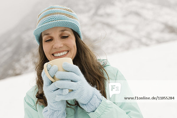 Eine Frau mit einer blauen Strickmütze mit Handschuhen  die eine Tasse Kaffee hält.