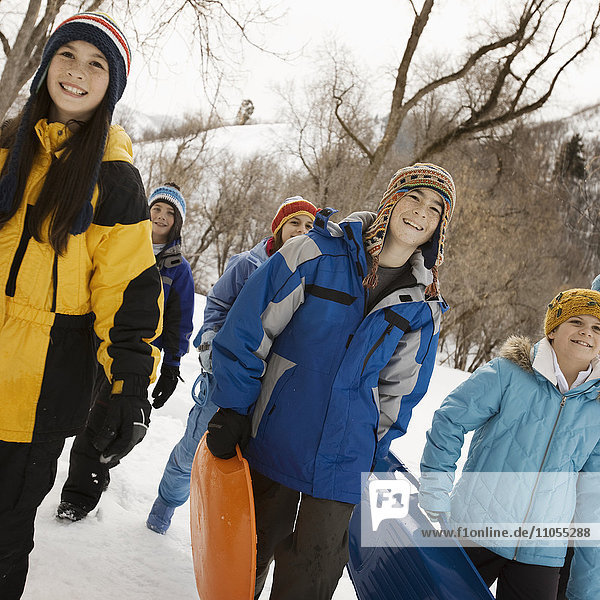 Eine Gruppe von Kindern  Jungen und Mädchen  die Schlitten über den Schnee tragen.