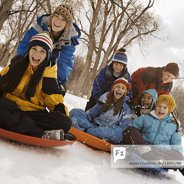A group of children  boys and girls  riding on sledges on the snow.