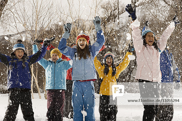 Eine Gruppe Jugendlicher  Jungen und Mädchen im Freien  die unter dem fallenden Schnee lachend die Arme heben