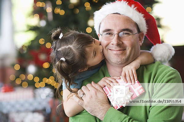 Ein Mann und ein Mädchen  Vater und Tochter  umarmen sich und tauschen an einem Weihnachtsbaum Geschenke aus.