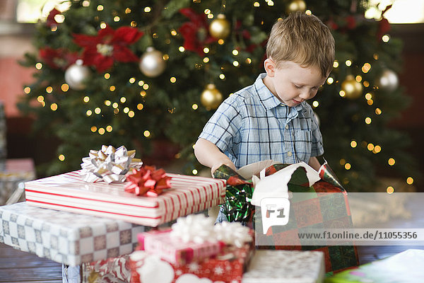 Ein Kind sitzt an einem Weihnachtsbaum und packt ein Paket aus.