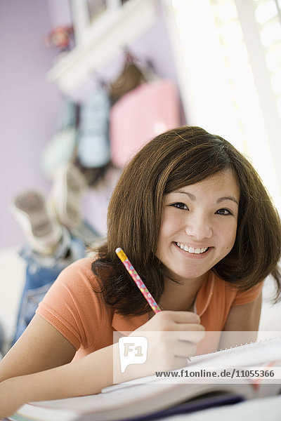 Ein Mädchen liegt auf ihrem Bett und hält einen Bleistift und ein Notizbuch in der Hand.