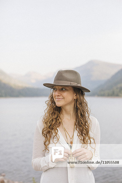 Eine Frau mit breitkrempigem Hut an einem Bergsee.