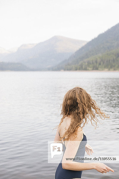 A woman in a black swimsuit wading into a calm lake in the mountains.