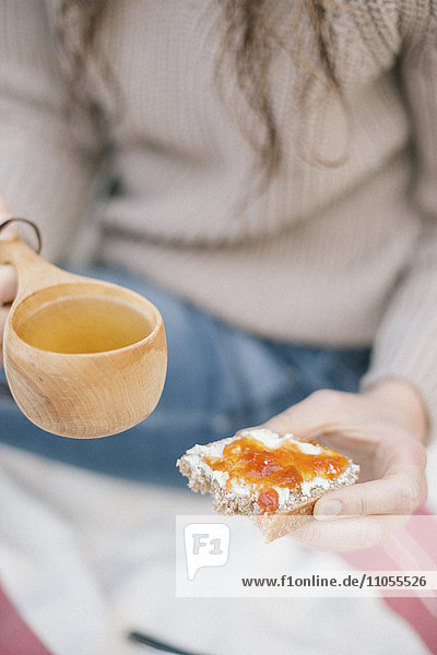 Eine Frau hält eine Tasse Tee und eine Scheibe Brot und Marmelade in der Hand.