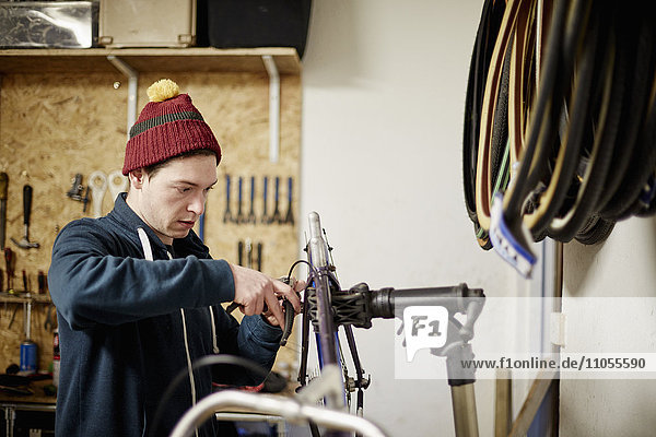 Ein junger Mann  der in einem Fahrradgeschäft arbeitet und ein Fahrrad repariert.