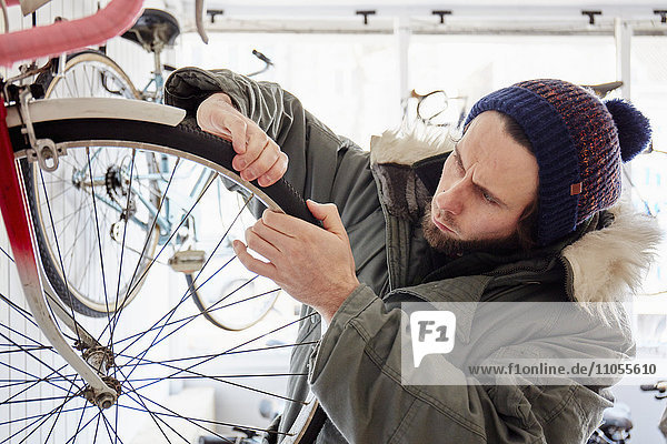 Ein junger Mann  der in einem Fahrradgeschäft arbeitet und ein Fahrrad repariert.