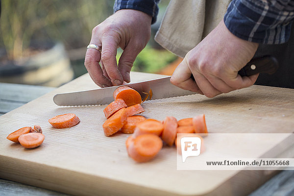 Ein Mann  der mit einem Messer Gemüse auf einem Brett schneidet und Karotten in Scheiben schneidet. .