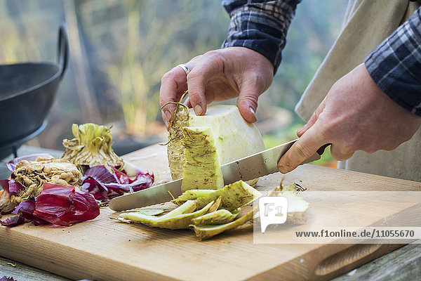 Ein Mann schneidet mit einem Messer Gemüse auf einem Brett und schält Sellerie.