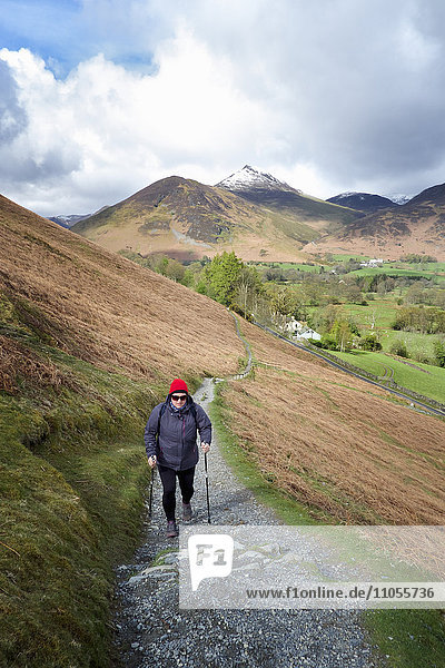 A woman walking up a path on a hillside in the Lake District with a trekking pole.