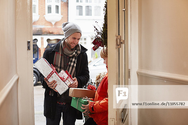 A man standing on a house doorstep with a stack of Christmas presents.