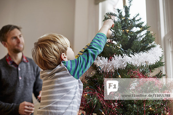 Ein Mann und ein Junge schmücken gemeinsam einen Weihnachtsbaum.