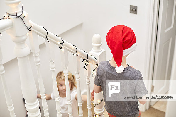 Ein Junge und ein Mädchen eilen am Weihnachtsmorgen die Treppe hinunter  einer trägt einen Weihnachtsmannhut.