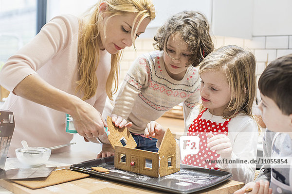 A woman and three children creating a baked gingerbread house.