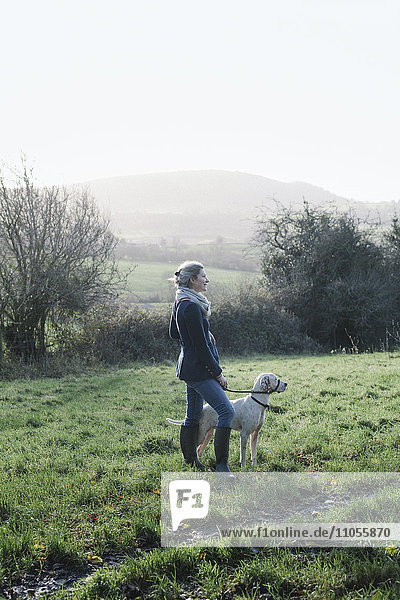 Eine Frau geht mit einem Hund auf einer Anhöhe mit Blick auf die Landschaft spazieren.