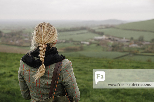 Eine Frau steht auf einer Bergkuppe und betrachtet die Aussicht.