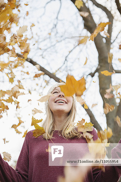 Ein jugendliches Mädchen im Freien  das Herbstblätter in die Luft wirft.