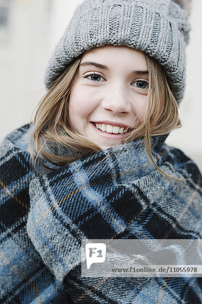 Ein junges Mädchen mit Schottenkaro-Schal und Wollmütze im Winter im Freien.