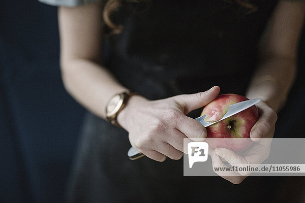 Eine Frau in einer blauen Schürze schält einen Apfel mit einem Messer.