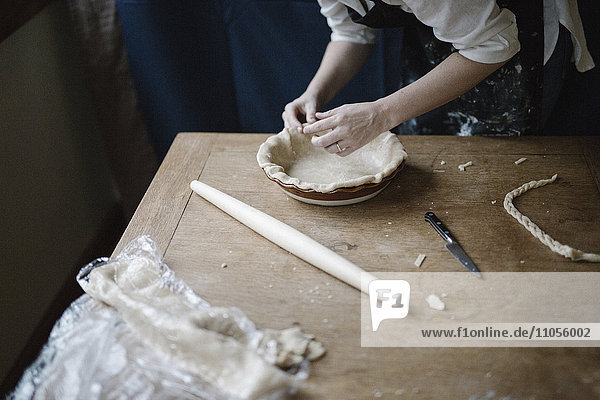 Eine Frau arbeitet daran  den Rand einer Konditoreihülle zu glätten  die eine Kuchenform auskleidet.