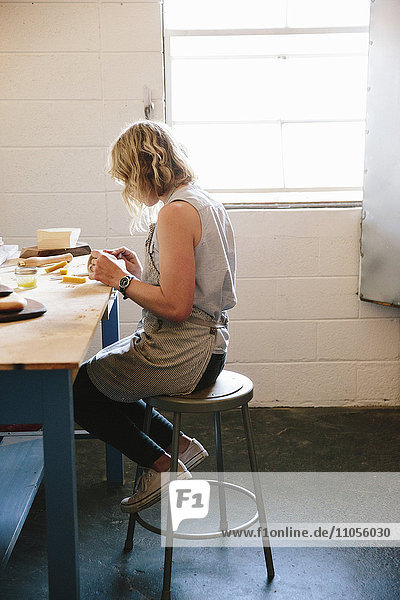 Eine Frau sitzt auf einem Hocker in einer Werkstatt.