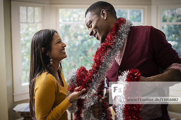 A young couple hanging tinsel up  decorating a house at Christmas.