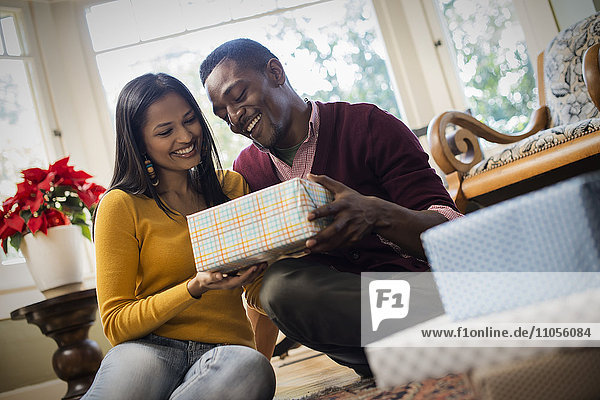 A couple on a sofa  exchanging wrapped presents.