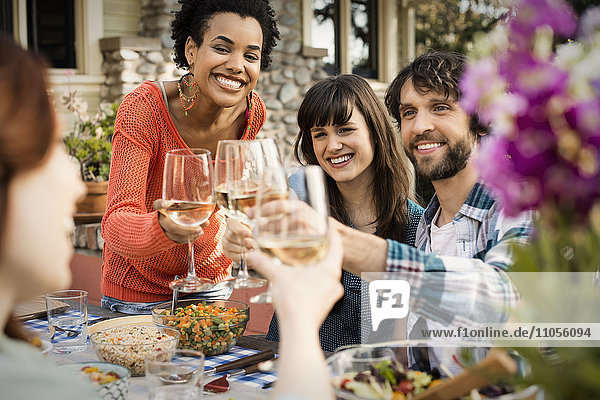 Freunde an einem Tisch  Männer und Frauen lachen und stoßen mit einem Weinglas an.