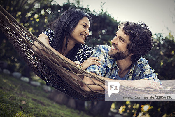 Ein Paar  ein junger Mann und eine Frau liegen in einer großen Hängematte im Garten.