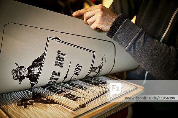 Ein Schildermaler  der ein Blatt bedruckter Karte von einer ausgeschnittenen Linoleum-Oberfläche  einem Holzschnitt  abhebt.