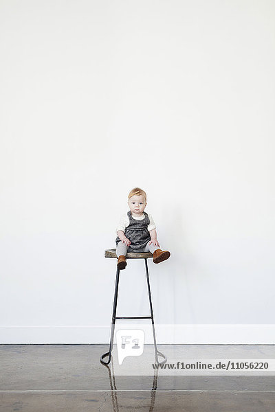Ein kleines Kind,  ein kleines Mädchen,  das lachend auf einem hohen Hocker sitzt.