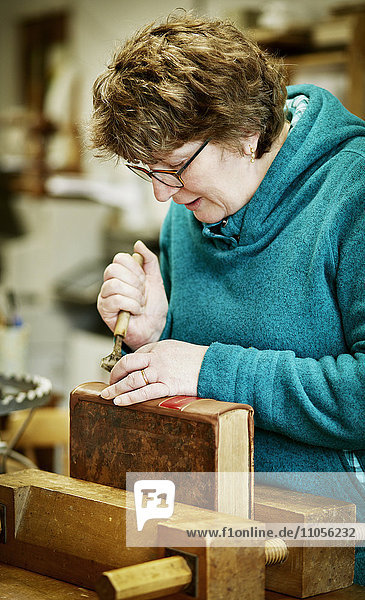 Eine Frau  die mit einem Handwerkzeug am Rücken eines gebundenen Buches arbeitet.