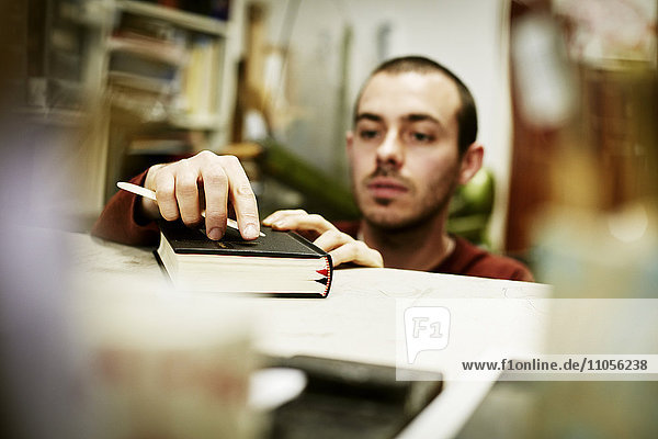 Ein Mann  der ein Handwerkzeug auf dem Einband eines Buches benutzt.