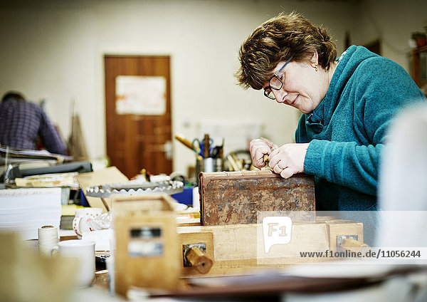 Eine Frau arbeitet an einer Bank am Einband eines restaurierungsbedürftigen Buches.