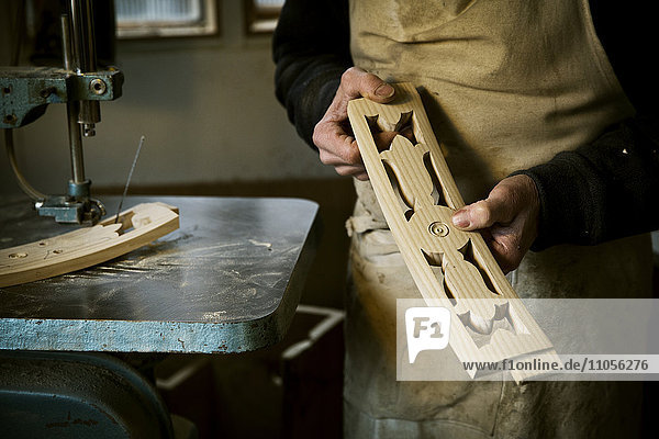 Ein Mann  der in der Werkstatt eines Möbelherstellers arbeitet  hält geformte geschnitzte Stuhllehnenstreben in der Hand.