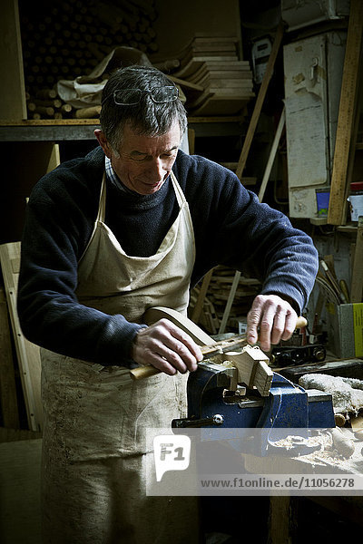 Ein Mann arbeitet in der Werkstatt eines Möbelherstellers und schleift ein Stück Holz  das in einer Klemme gehalten wird.