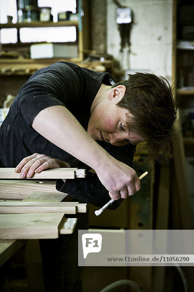 Eine Frau  die in der Werkstatt eines Möbelherstellers arbeitet und mit einem kleinen Pinsel Leim auf das Holz aufträgt.
