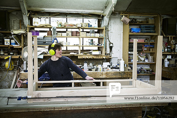 Eine Frau  die in der Werkstatt eines Möbelherstellers arbeitet und einen Tisch zusammenbaut.